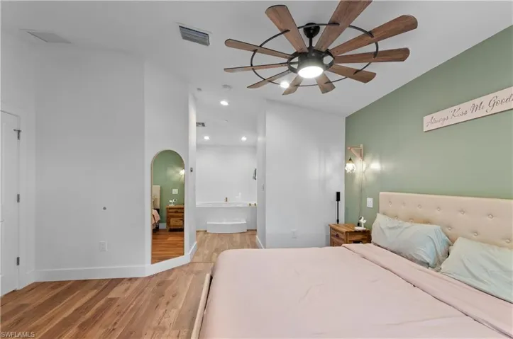 Bedroom with light wood finished floors, recessed lighting, arched walkways, ensuite bathroom, and a ceiling fan