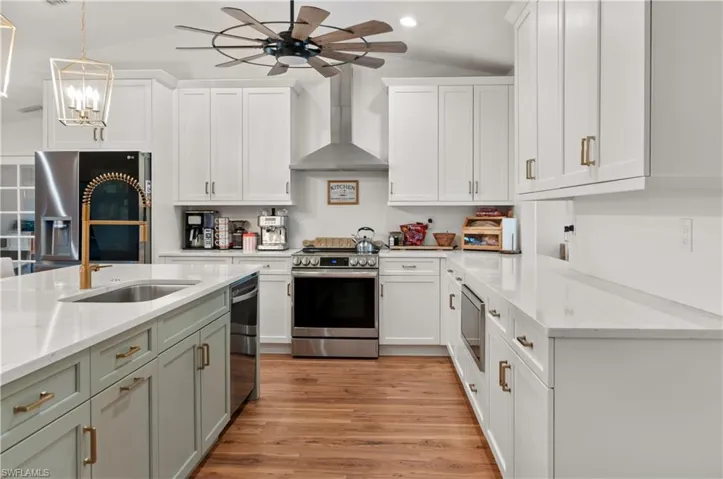 Kitchen featuring white cabinets, light stone countertops, stainless steel appliances, pendant lighting, and wall chimney range hood