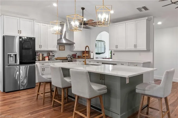 Kitchen featuring stainless steel fridge with ice dispenser, white cabinets, arched walkways, pendant lighting, and wall chimney range hood
