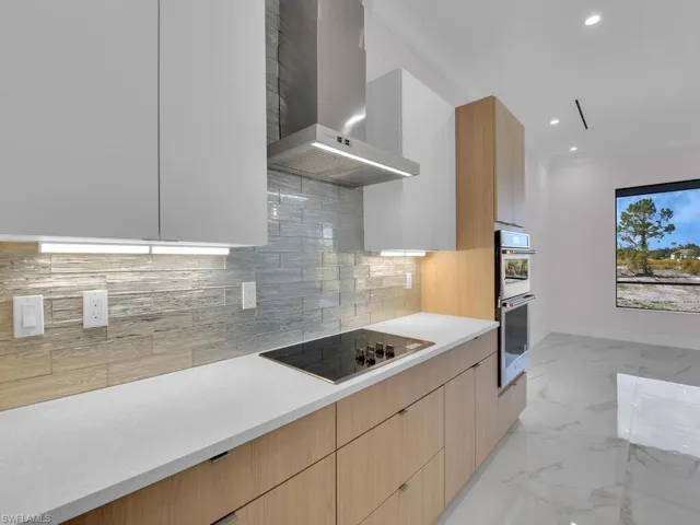 Kitchen with decorative backsplash, black electric stovetop, light brown cabinetry, stainless steel double oven, and wall chimney range hood