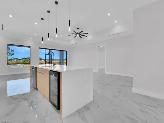 Kitchen featuring ceiling fan, beverage cooler, sink, pendant lighting, and an island with sink