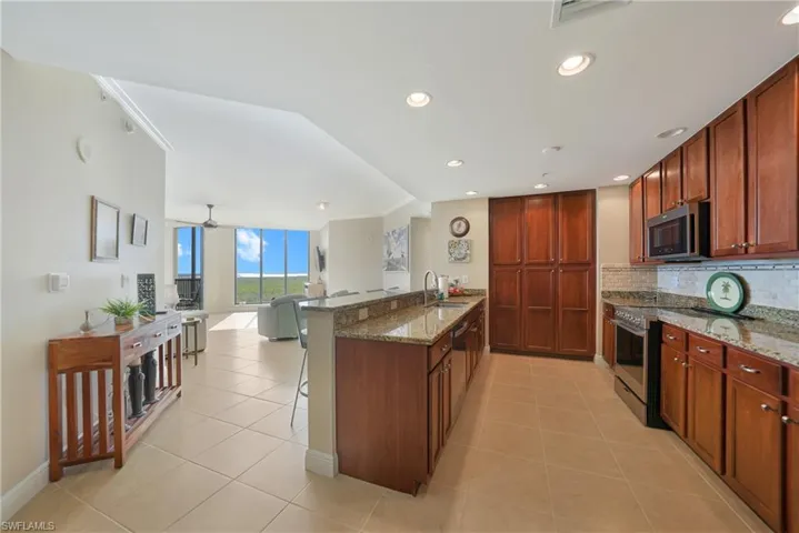 Kitchen with dark stone counters, light tile patterned floors, stainless steel appliances, expansive windows, and tasteful backsplash