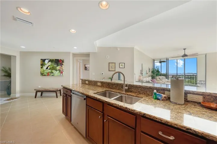 Kitchen with stainless steel dishwasher, light stone counters, brown cabinetry, open floor plan, and recessed lighting