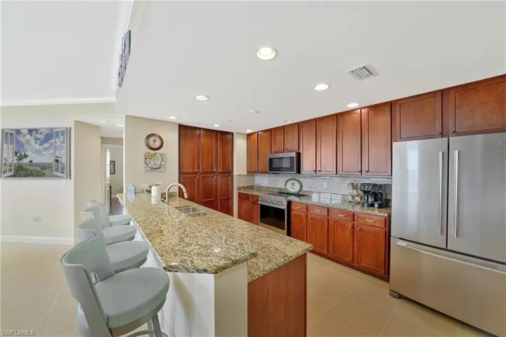 Kitchen with appliances with stainless steel finishes, light stone countertops, a kitchen breakfast bar, light tile patterned flooring, and a peninsula