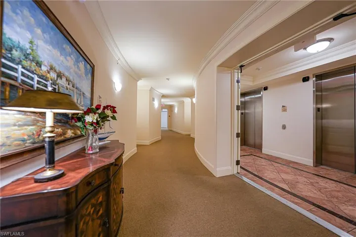 Hall featuring elevator, crown molding, inlaid floor details, and light carpet