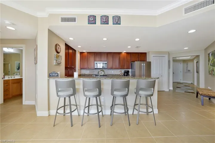 Kitchen with a kitchen bar, a peninsula, light stone counters, appliances with stainless steel finishes, and light tile patterned floors