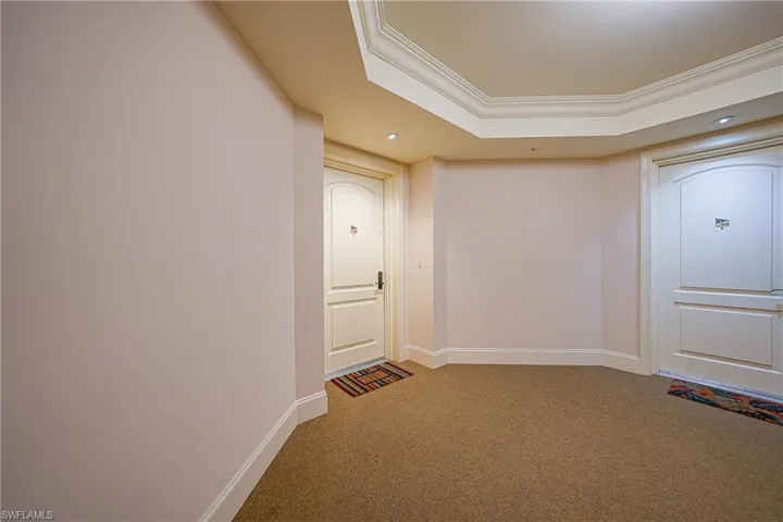 Hallway with ornamental molding, light carpet, recessed lighting, and a tray ceiling