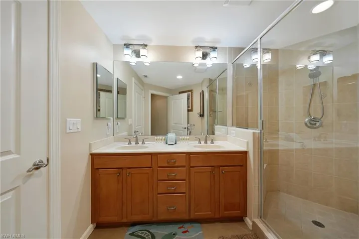 Bathroom with double vanity, a shower stall, and light tile patterned floors