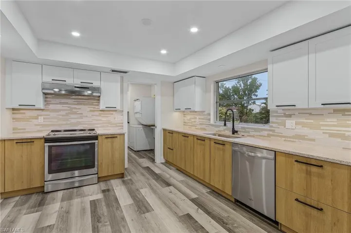 Kitchen featuring stacked washer / drying machine, sink, appliances with stainless steel finishes, light hardwood / wood-style floors, and white cabinets