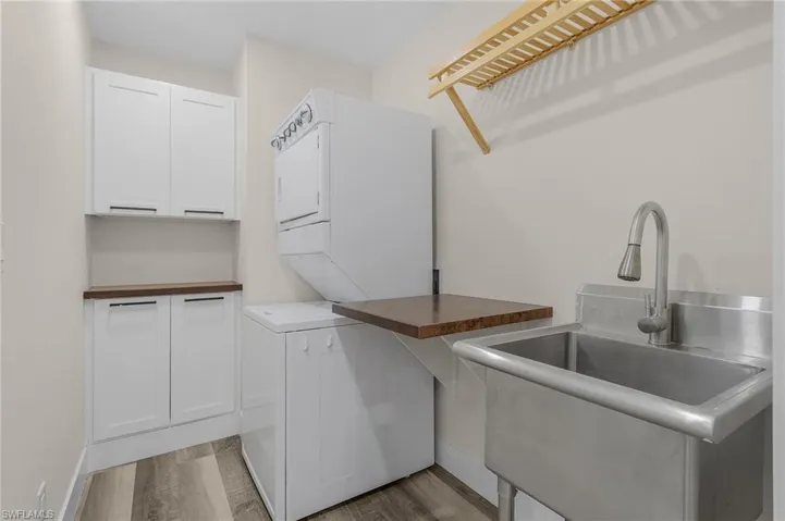 Laundry room with cabinets, stacked washer / drying machine, sink, and light hardwood / wood-style floors