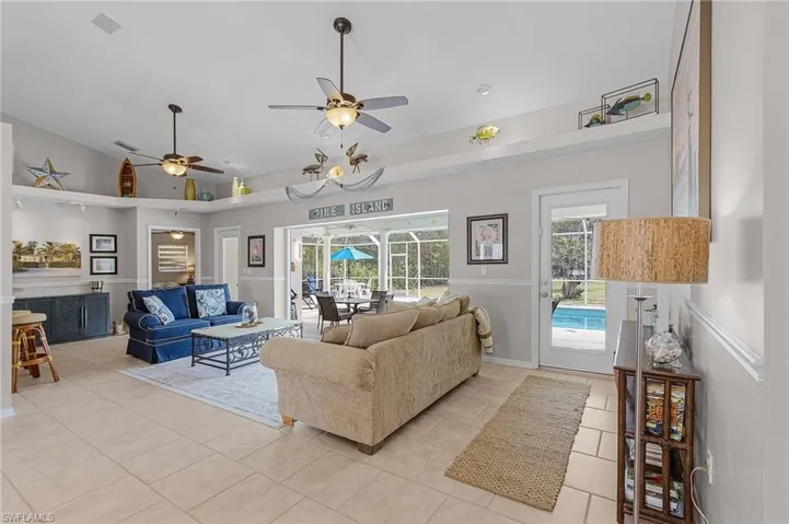 Open living room with high ceilings, decorative shelving, and tile floors.  Pocket sliding glass doors open out to the covered sitting area by the pool.  There are 2 additional doors leading out to the screened pool.