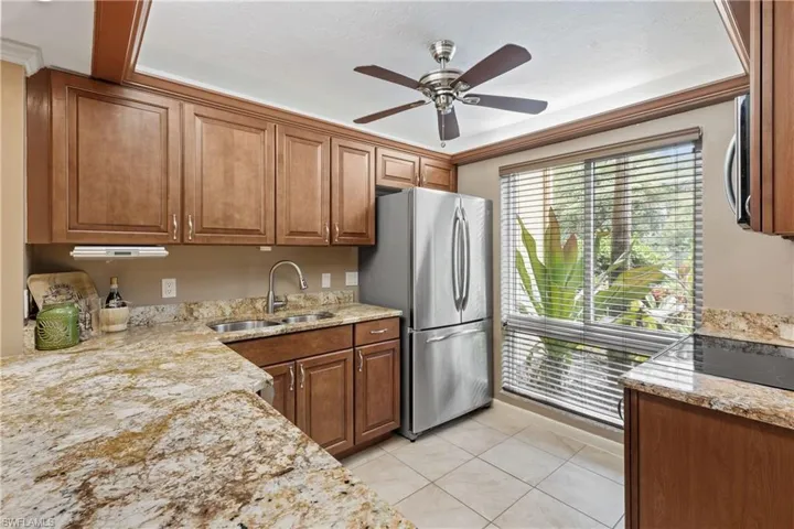 Kitchen featuring appliances with stainless steel finishes, light stone countertops, light tile patterned floors, ceiling fan, and sink