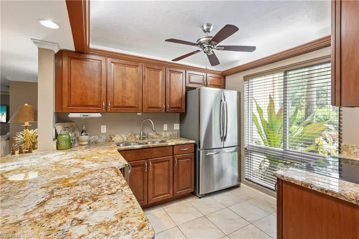 Kitchen with ceiling fan, sink, stainless steel refrigerator, light stone countertops, and crown molding