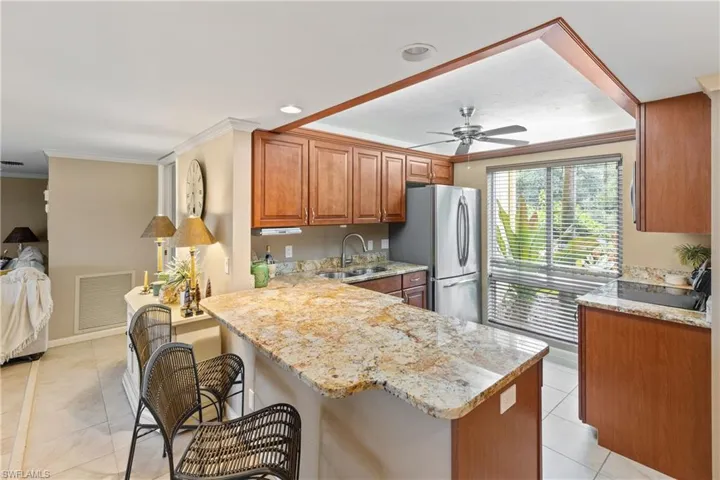 Kitchen featuring light stone counters, sink, kitchen peninsula, ceiling fan, and stainless steel fridge