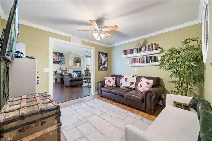 Living area with wood finished floors, ceiling fan, ornamental molding, and a glass covered fireplace