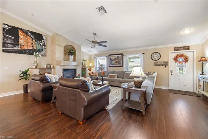 Living room featuring crown molding, a tiled fireplace, dark wood-style flooring, and a ceiling fan