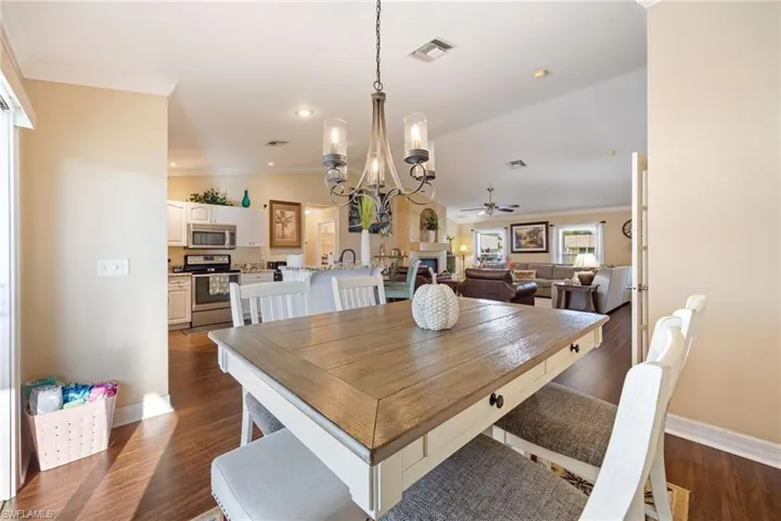 Dining space with crown molding, a chandelier, dark wood-style flooring, a fireplace, and recessed lighting