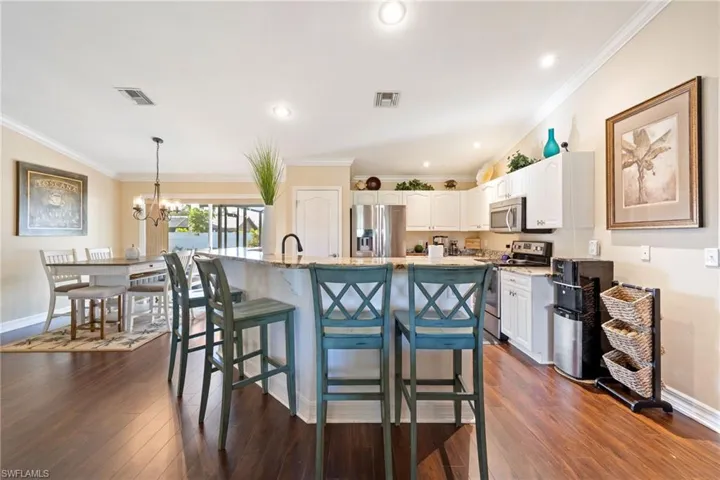 Kitchen with white cabinets, a breakfast bar, stainless steel appliances, ornamental molding, and light stone countertops