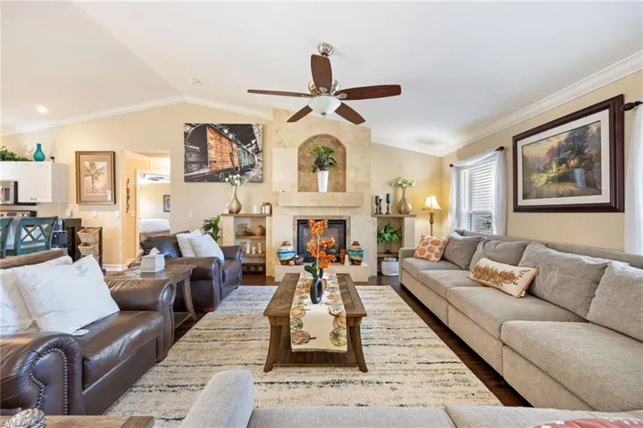 Living area with vaulted ceiling, ornamental molding, a tile fireplace, a ceiling fan, and wood finished floors