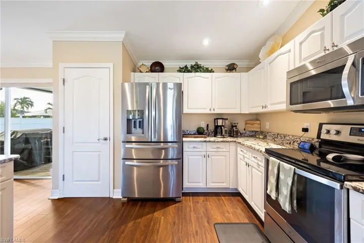 Kitchen featuring appliances with stainless steel finishes, light stone countertops, white cabinetry, crown molding, and dark wood-style floors