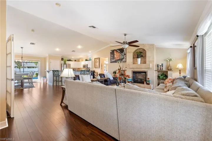 Living room featuring crown molding, dark wood-style floors, a tiled fireplace, vaulted ceiling, and ceiling fan