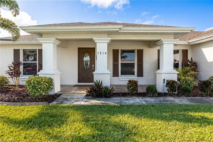 Entrance to property with a porch, a yard, stucco siding, and roof with shingles