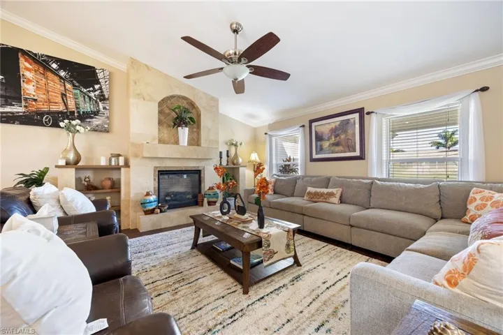 Living room with ornamental molding, a premium fireplace, a ceiling fan, vaulted ceiling, and wood finished floors