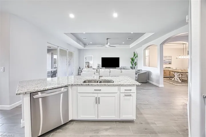 Kitchen with white cabinets, light stone countertops, a tray ceiling, dishwasher, and sink
