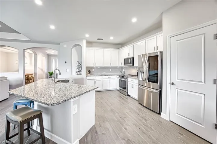 Kitchen with appliances with stainless steel finishes, an island with sink, light hardwood / wood-style floors, white cabinets, and light stone counters