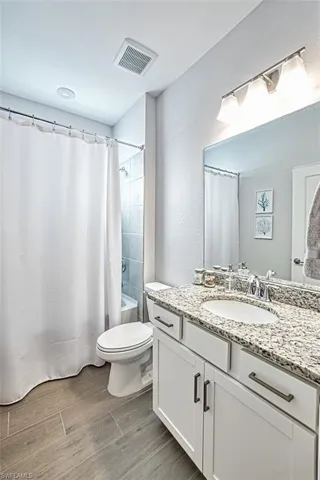 Full bathroom featuring vanity, shower / bath combo with shower curtain, hardwood / wood-style flooring, and toilet