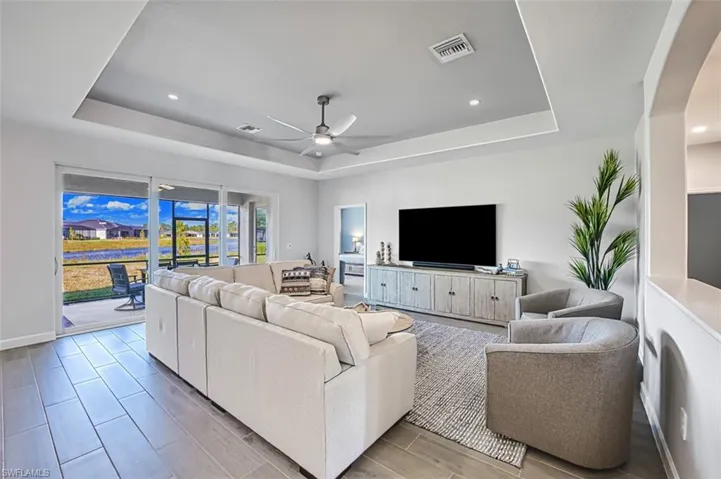 Living room with ceiling fan, a tray ceiling, and light hardwood / wood-style flooring