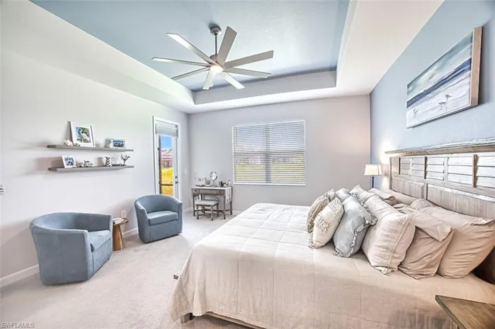 Bedroom with ceiling fan, light carpet, and a tray ceiling