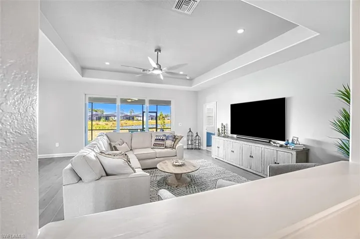 Living room featuring ceiling fan, a tray ceiling, and light wood-type flooring