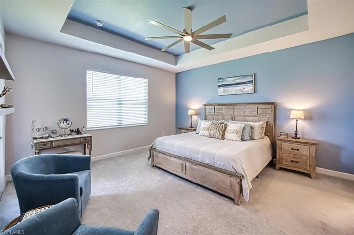 Bedroom featuring a raised ceiling, light colored carpet, and ceiling fan