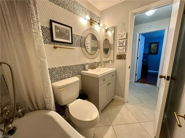 Bathroom featuring a clawfoot tub with shower, contemporary vanity with an integrated sink, patterned mosaic tile accent wall, and large format floor tiling