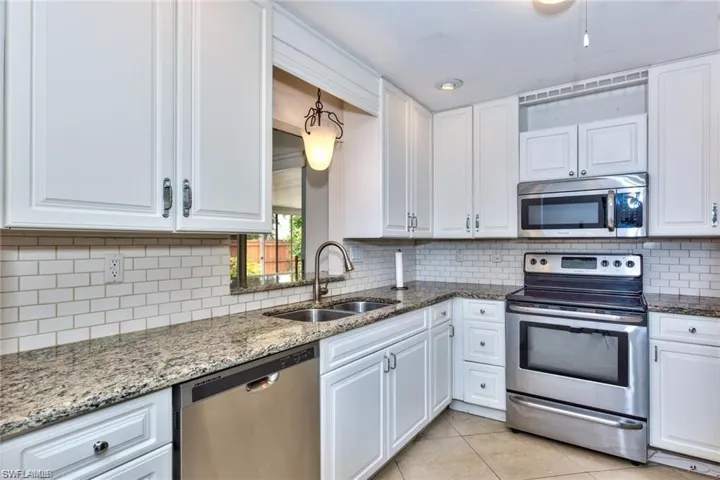 Kitchen featuring white shaker-style cabinetry, granite countertops, subway tile backsplash, stainless steel appliances, and a double basin sink with a gooseneck faucet
