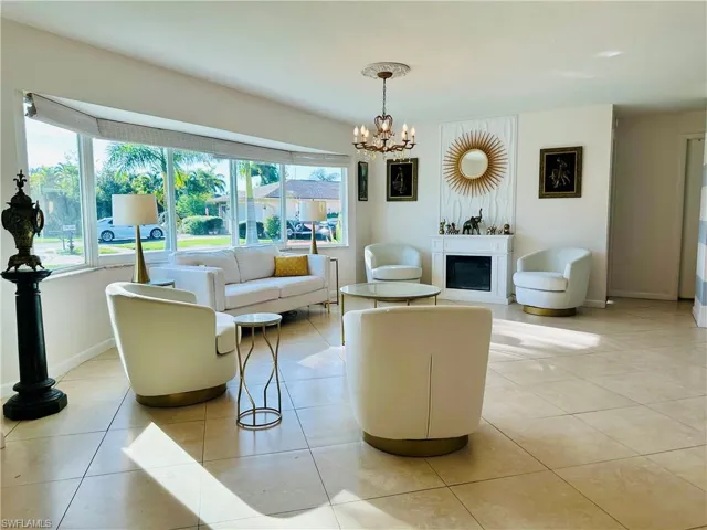 Spacious living area featuring large bay windows, neutral tile flooring, a decorative fireplace, and a chandelier with a ceiling medallion