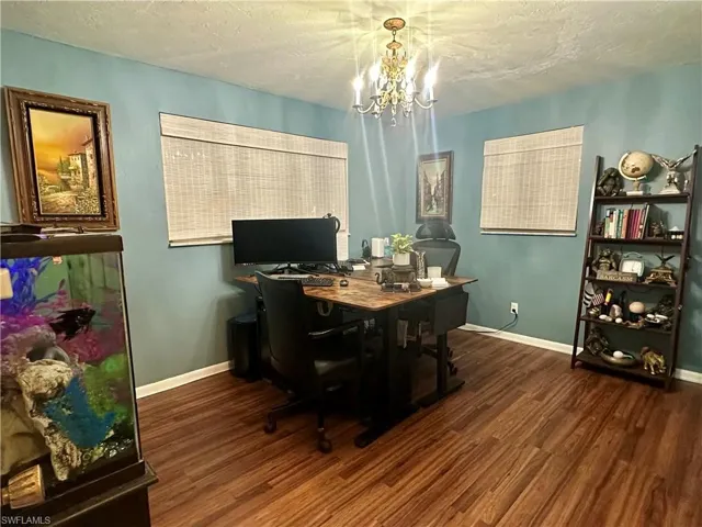 Room featuring rich wood-finish flooring, light blue wall paint, two windows with woven blinds, and a chandelier light fixture
