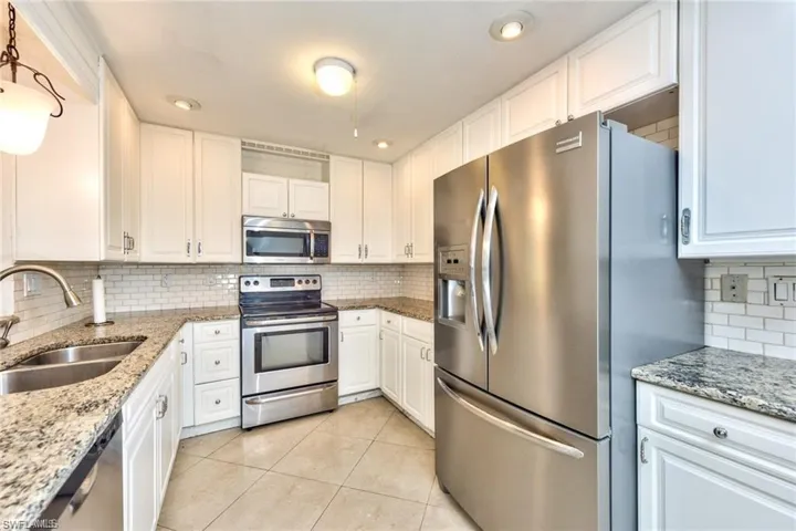 Kitchen featuring abundant white cabinetry, stainless steel appliances, granite countertops, subway tile backsplash, and tile flooring