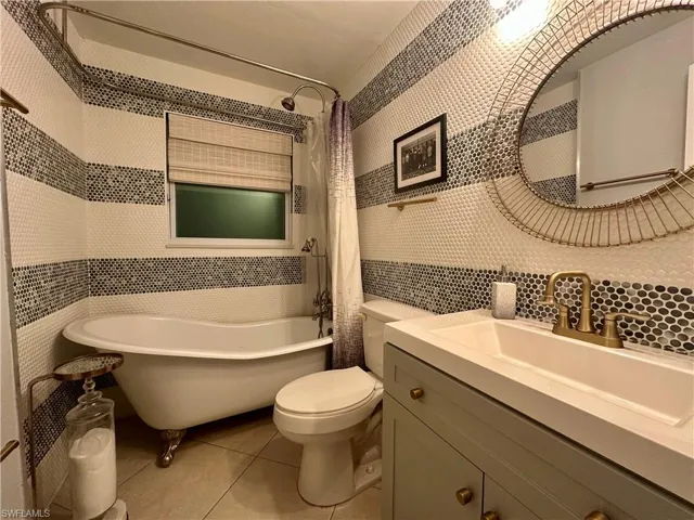 Bathroom featuring a clawfoot tub, striped mosaic tile wall, and a single vanity with a bronze-tone faucet