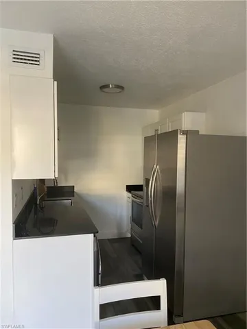 Kitchen featuring fridge, white cabinetry, dark countertops, a textured ceiling, and stove