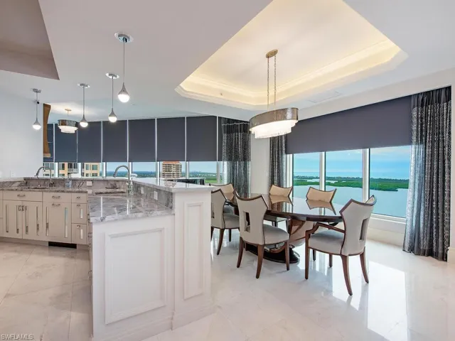 Kitchen with light stone countertops, hanging light fixtures, a raised ceiling, and a water view