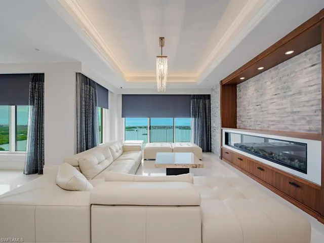 Living area featuring a glass covered fireplace, a tray ceiling, healthy amount of natural light, ornamental molding, and a chandelier