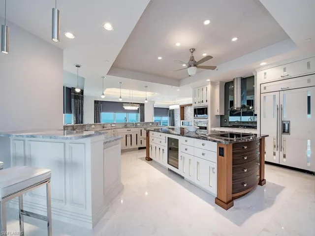 Kitchen featuring a raised ceiling, decorative light fixtures, dark stone countertops, white cabinets, and built in appliances