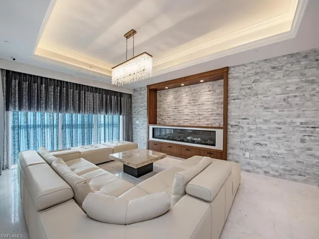 Living area with a tray ceiling, a glass covered fireplace, crown molding, and a chandelier