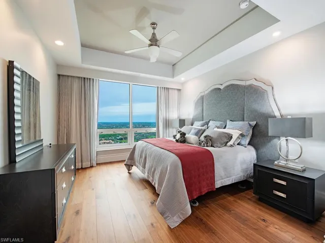 Bedroom with a tray ceiling, ceiling fan, light wood finished floors, and recessed lighting