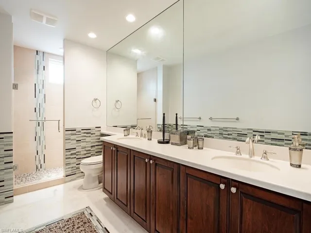 Full bath featuring double vanity, a shower stall, recessed lighting, and tile walls