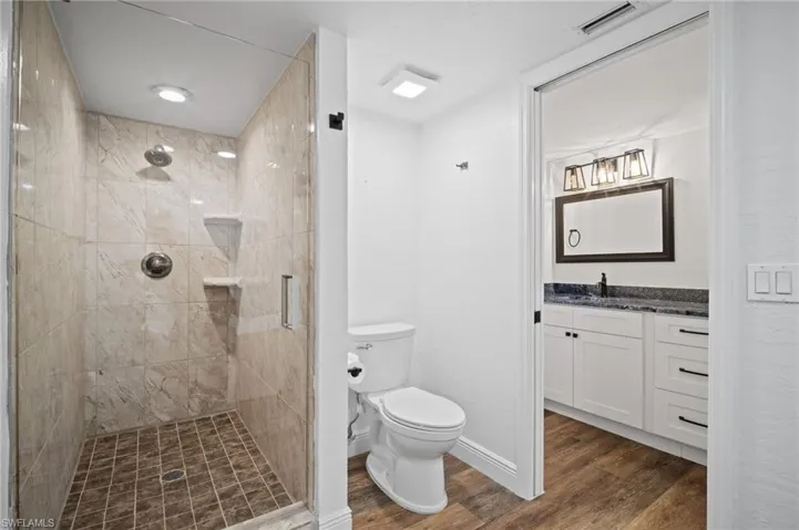 Full bath with a stall shower, vanity, and dark wood-style floors