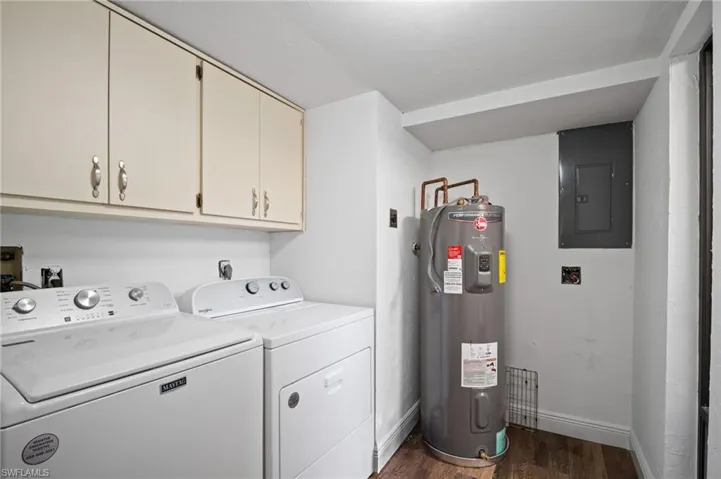 Laundry area with dark wood-type flooring, electric panel, water heater, washer and clothes dryer, and cabinet space