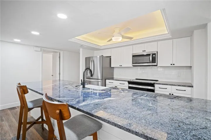Kitchen with a tray ceiling, backsplash, wood finished floors, white cabinetry, and recessed lighting